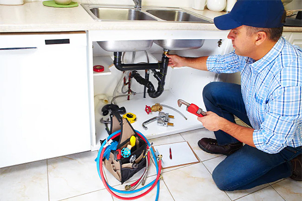 Loodgieter die leidingen onder een keukengootsteen herstelt met professioneel gereedschap